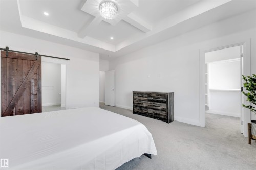 Spacious room featuring a tray ceiling with a modern chandelier and recessed lighting, plush carpeting, a rustic wood barn door, and a built-in closet with shelving - 1923 19 Avenue, Edmonton, AB - Indoor Photo Showing Bedroom