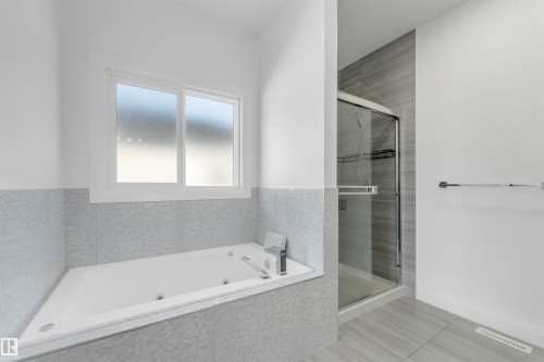 Spacious bathroom featuring a built-in jetted tub with tile surround, a separate glass-enclosed shower with a sliding door, and light gray tile flooring - 1923 19 Avenue, Edmonton, AB - Indoor Photo Showing Bathroom