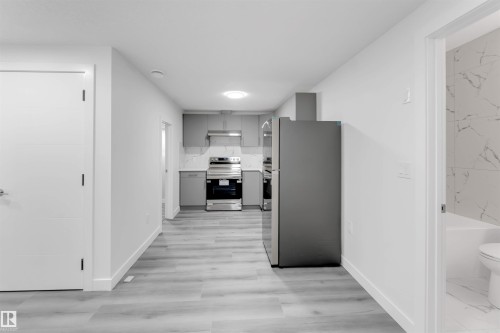 Modern kitchen area featuring grey cabinetry, stainless steel appliances, and a marble-patterned backsplash - 1923 19 Avenue, Edmonton, AB - Indoor