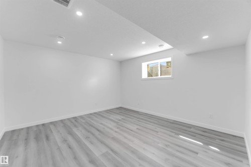 Spacious room featuring light wood-finish flooring, recessed lighting, white walls, and a window - 1923 19 Avenue, Edmonton, AB - Indoor Photo Showing Other Room