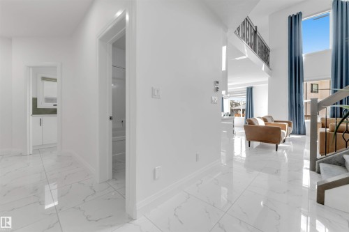 Bright interior space featuring polished white tile flooring, tall ceilings, and a modern stair railing - 1923 19 Avenue, Edmonton, AB - Indoor Photo Showing Other Room
