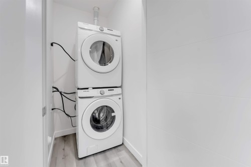 Dedicated laundry area featuring a stacked washer and dryer, light wood-finish flooring, and crisp white walls - 1923 19 Avenue, Edmonton, AB - Indoor Photo Showing Laundry Room