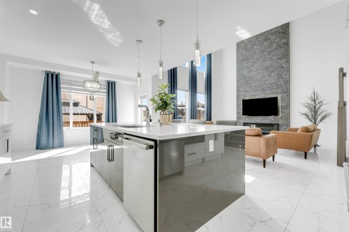 Open-concept living space with large format marble-look tile flooring, a kitchen island featuring a white countertop and high-gloss cabinetry, and a floor-to-ceiling stacked stone fireplace surround - 1923 19 Avenue, Edmonton, AB - Indoor Photo Showing Kitchen With Upgraded Kitchen
