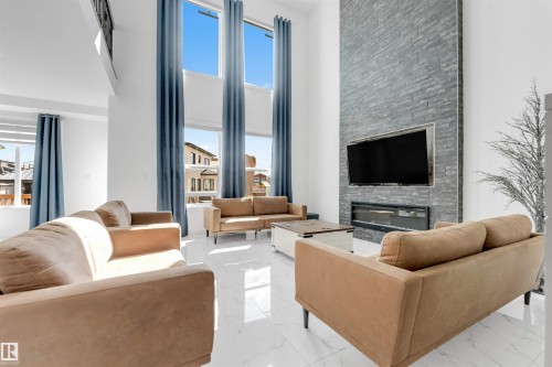 Spacious living area featuring a two-story ceiling, tall windows with blue drapes, and white tile flooring - 1923 19 Avenue, Edmonton, AB - Indoor Photo Showing Living Room With Fireplace