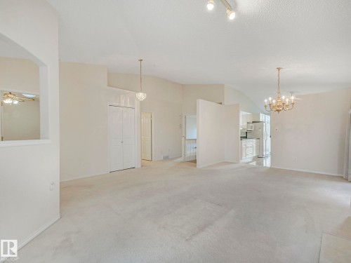 Vaulted ceilings enhance this carpeted living area, featuring a decorative chandelier and a contemporary pendant light fixture - 23 9731 174 Street, Edmonton, AB - Indoor