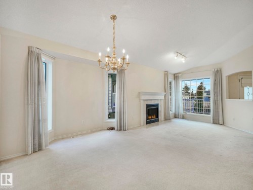 Spacious living area featuring a fireplace with a tiled surround, an elegant chandelier, multiple large windows, and an arched pass-through window with decorative glass - 23 9731 174 Street, Edmonton, AB - Indoor Photo Showing Living Room With Fireplace