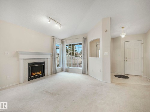 Living area featuring a fireplace with a white mantel, bay windows, and carpet flooring - 23 9731 174 Street, Edmonton, AB - Indoor Photo Showing Living Room With Fireplace