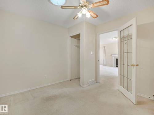 Carpeted room featuring a ceiling fan with integrated lighting, a built-in closet, and a glass-paneled door - 23 9731 174 Street, Edmonton, AB - Indoor Photo Showing Other Room
