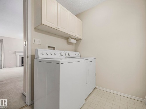 Laundry area featuring overhead cabinetry, light-toned wall paint, and grid-patterned floor tiling - 23 9731 174 Street, Edmonton, AB - Indoor Photo Showing Laundry Room