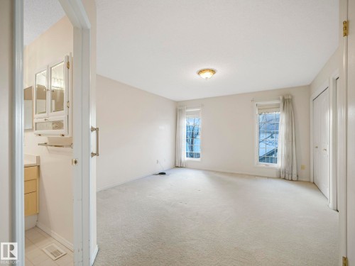 Spacious room featuring light-toned carpeting, two windows with white trim, and a flush-mount ceiling light fixture - 23 9731 174 Street, Edmonton, AB - Indoor Photo Showing Other Room