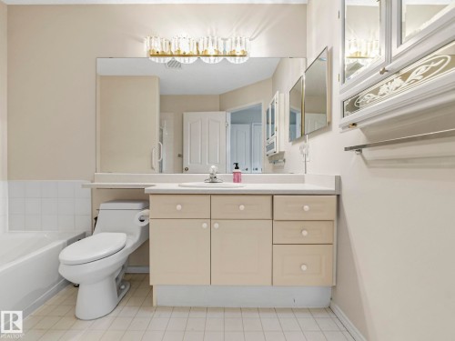 Bathroom featuring a single vanity with light cabinetry, a large mirror, a chrome faucet, and a wall-mounted light fixture - 23 9731 174 Street, Edmonton, AB - Indoor Photo Showing Bathroom