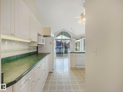 Kitchen featuring white cabinetry, green countertops, patterned flooring, and an arched window overlooking a deck - 23 9731 174 Street, Edmonton, AB - Indoor Photo Showing Kitchen