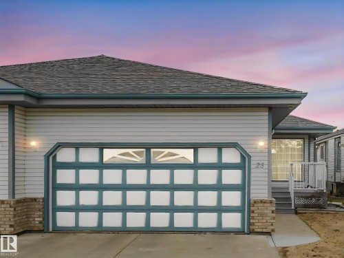 Exterior featuring light-colored siding with dark trim, a prominent garage door with window inserts, and brick accents - 23 9731 174 Street, Edmonton, AB - Outdoor