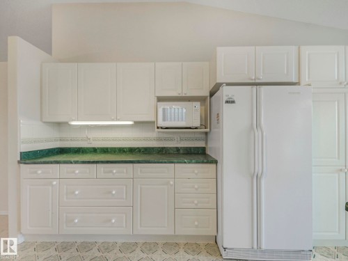 Kitchen featuring white cabinetry, green stone-finish countertops, white subway tile backsplash, and under-cabinet lighting - 23 9731 174 Street, Edmonton, AB - Indoor
