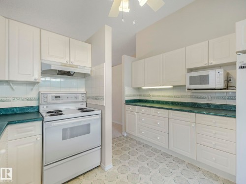 Kitchen featuring white cabinetry, a built-in microwave, white electric range with a coordinating range hood, vaulted ceiling, and patterned flooring - 23 9731 174 Street, Edmonton, AB - Indoor Photo Showing Kitchen