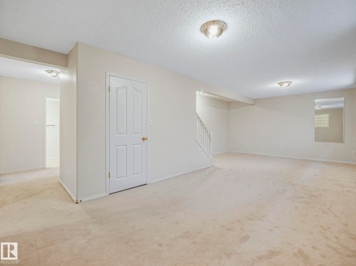 Spacious room featuring neutral carpet flooring, recessed ceiling lighting, a paneled door, and a staircase with white balusters - 23 9731 174 Street, Edmonton, AB - Indoor Photo Showing Other Room
