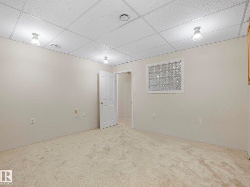 Carpeted room featuring a white drop ceiling with flush-mount lighting, light beige walls, and a glass block window - 23 9731 174 Street, Edmonton, AB - Indoor Photo Showing Other Room