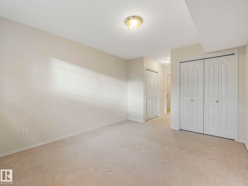 Spacious carpeted room featuring bi-fold closet doors, cream-painted walls, and ceiling-mounted light fixtures - 23 9731 174 Street, Edmonton, AB - Indoor Photo Showing Other Room