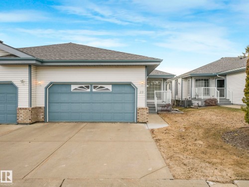 Exterior featuring light-colored siding with brick accents, an attached garage with a blue door, and a concrete driveway - 23 9731 174 Street, Edmonton, AB - Outdoor