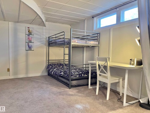 Carpeted room featuring panel walls, a suspended ceiling, and two upper windows providing natural light - 11681 72 Avenue, Edmonton, AB - Indoor Photo Showing Bedroom