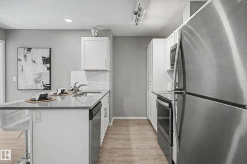 Modern kitchen featuring wood-finish flooring, white cabinetry, stainless steel appliances, and a tile backsplash - 217 394 Windermere Road, Edmonton, AB - Indoor Photo Showing Kitchen With Stainless Steel Kitchen With Upgraded Kitchen