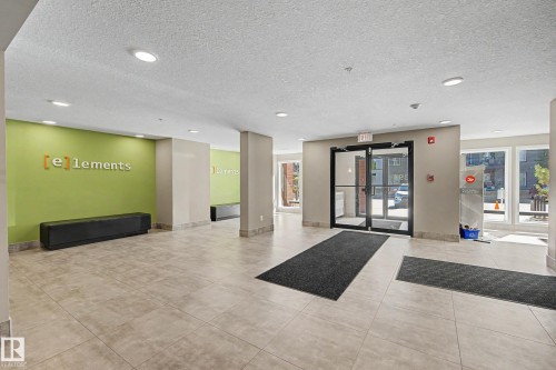 Spacious lobby featuring large format tile flooring, recessed lighting, double glass entry doors, and a decorative accent wall - 217 394 Windermere Road, Edmonton, AB - Indoor Photo Showing Other Room