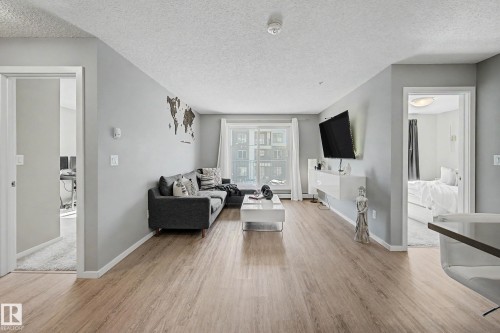 Spacious living area featuring light wood-finish flooring, light grey painted walls, and white trim - 217 394 Windermere Road, Edmonton, AB - Indoor Photo Showing Living Room