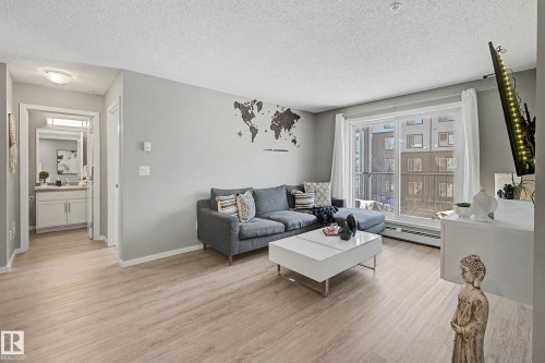 Living area featuring light wood-finish flooring, a sliding glass door to a balcony, and light gray walls - 217 394 Windermere Road, Edmonton, AB - Indoor Photo Showing Living Room