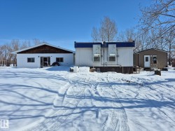 The property features a white structure with a brown shingled gable, a white and blue portable building, and a brown structure with a white door - 