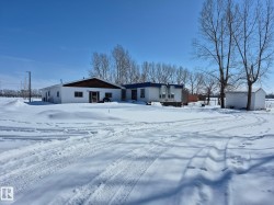 The property features a white exterior with a brown shingled roof and a detached shed - 