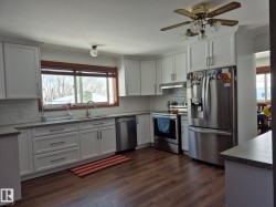 The kitchen features white cabinetry, stainless steel appliances, a tile backsplash, and a window above the sink - 