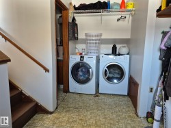 This laundry area features a washer and dryer, with shelving for storage, and access to an additional room - 