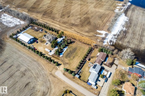 Expansive rural property featuring a main residence with a brown hip roof, a large white outbuilding with a gray roof, mature evergreen trees bordering the property, and a gravel driveway - 2B Discovery Avenue, Rural Sturgeon County, AB 