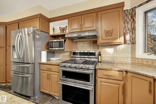 Kitchen featuring stainless steel appliances, light brown cabinetry, stone countertops, and a decorative tile backsplash - 33 Glen Meadow Crescent, St. Albert, AB - Indoor Photo Showing Kitchen