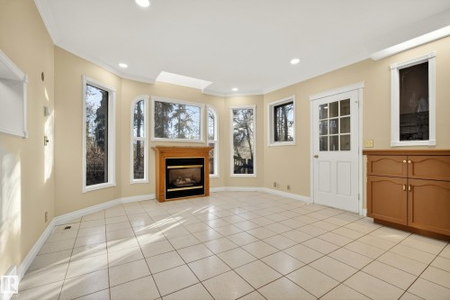 Spacious room featuring light-toned tile flooring and a gas fireplace with a wood-finish mantel and stone surround - 33 Glen Meadow Crescent, St. Albert, AB - Indoor With Fireplace