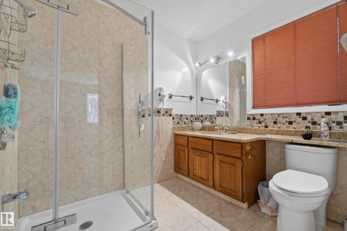 Bathroom featuring a glass-enclosed shower, light-toned tile work, a wood-finish vanity with a stone-finish countertop, and a mosaic tile backsplash - 33 Glen Meadow Crescent, St. Albert, AB - Indoor Photo Showing Bathroom