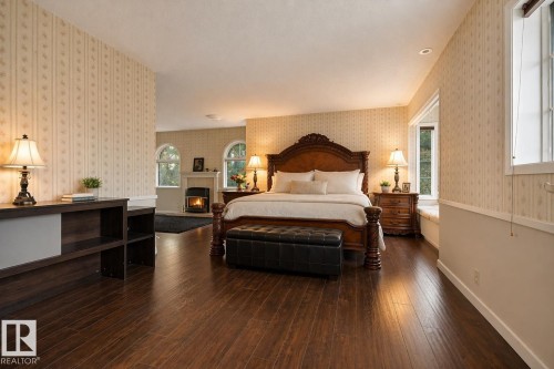 Spacious bedroom featuring dark wood-finish flooring, a fireplace with a stone hearth, and two arched windows - 33 Glen Meadow Crescent, St. Albert, AB - Indoor Photo Showing Bedroom