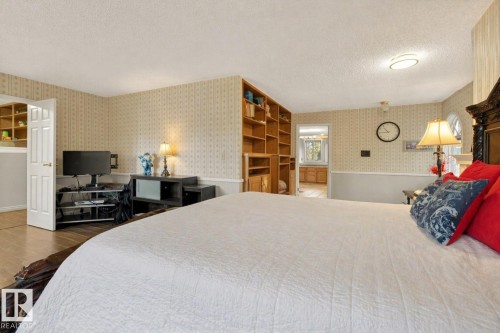 Bedroom featuring built-in wooden shelving, a white paneled door, and a two-tone wall treatment with patterned wallpaper and a lower wainscot - 33 Glen Meadow Crescent, St. Albert, AB - Indoor Photo Showing Bedroom