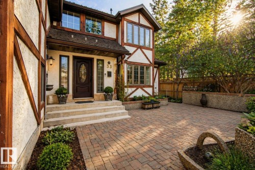 Tudor-style exterior with decorative half-timbering, a dark wood entry door featuring an oval leaded glass insert, and a brick paver driveway - 33 Glen Meadow Crescent, St. Albert, AB - Outdoor With Deck Patio Veranda