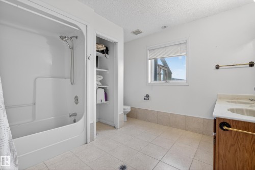 Bathroom featuring a white tub-shower combination, a dual-sink vanity with a wood-finish cabinet, and tiled flooring - 33 Glen Meadow Crescent, St. Albert, AB - Indoor Photo Showing Bathroom