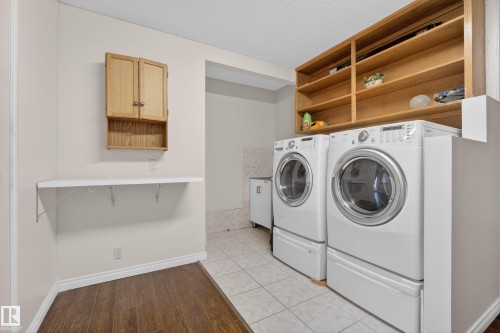 Dedicated laundry area featuring a front-loading washer and dryer, extensive built-in shelving, a wall-mounted folding shelf, and overhead cabinetry - 33 Glen Meadow Crescent, St. Albert, AB - Indoor Photo Showing Laundry Room