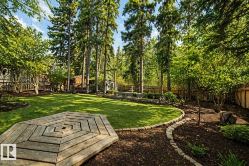 Expansive backyard featuring a central lawn, mature trees, a decorative wood-plank patio, and a sculpted stone-edged pathway - 33 Glen Meadow Crescent, St. Albert, AB - Outdoor