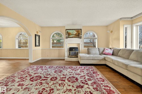 Living area featuring a white mantelpiece with a built-in fireplace, multiple arched windows, and wood-finish flooring - 33 Glen Meadow Crescent, St. Albert, AB - Indoor Photo Showing Living Room With Fireplace