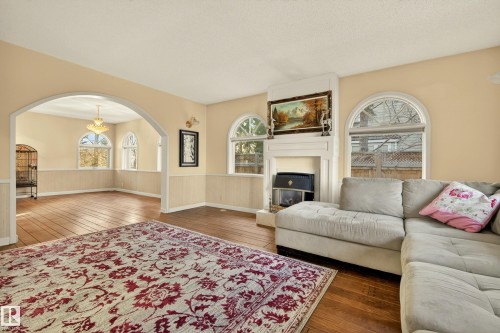 Living area featuring a fireplace with a mantel, arched windows, and wood-finish flooring - 33 Glen Meadow Crescent, St. Albert, AB - Indoor Photo Showing Living Room With Fireplace