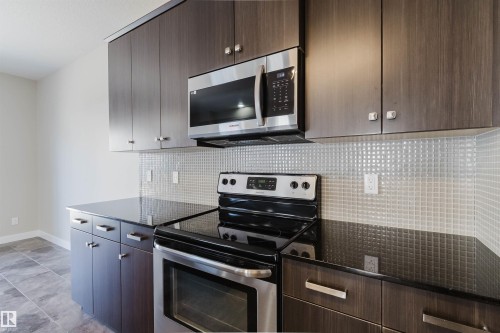 Modern kitchen featuring rich wood-finish cabinetry, dark countertops, and a full stainless steel appliance package, including a built-in microwave and electric range - 611 176 Street, Edmonton, AB - Indoor Photo Showing Kitchen
