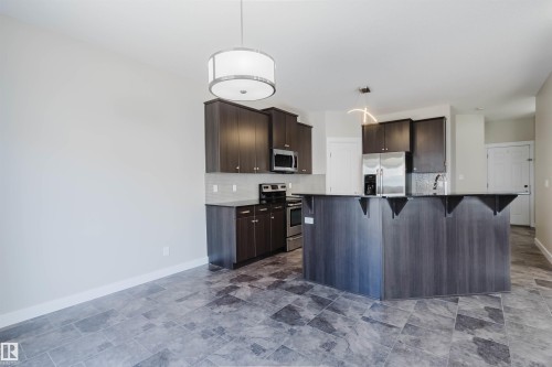 Spacious kitchen featuring dark wood-finish cabinetry, stainless steel appliances, and a central island with a breakfast bar - 611 176 Street, Edmonton, AB - Indoor Photo Showing Kitchen
