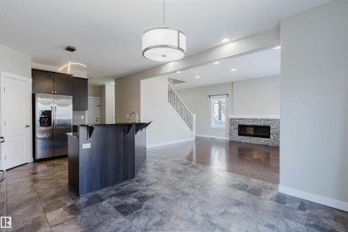 Kitchen featuring dark wood-finish cabinetry, stainless steel refrigerator, and a central island with sink - 611 176 Street, Edmonton, AB - Indoor Photo Showing Kitchen With Fireplace