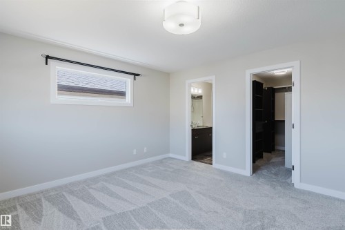 Carpeted room with a flush mount ceiling light, a high horizontal window, and two open doorways revealing a bathroom and a closet with built-in dark shelving - 611 176 Street, Edmonton, AB - Indoor