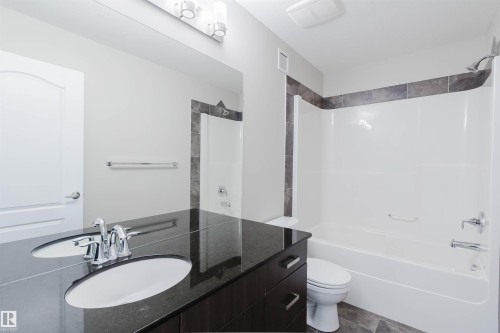 Bathroom featuring a dark wood-finish vanity with a built-in sink, a large mirror, a chrome faucet, a white bathtub, and a tiled shower surround - 611 176 Street, Edmonton, AB - Indoor Photo Showing Bathroom