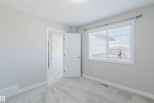 Neutral wall paint with light gray carpeting, featuring a large window with blinds and a white interior door - 611 176 Street, Edmonton, AB - Indoor Photo Showing Other Room